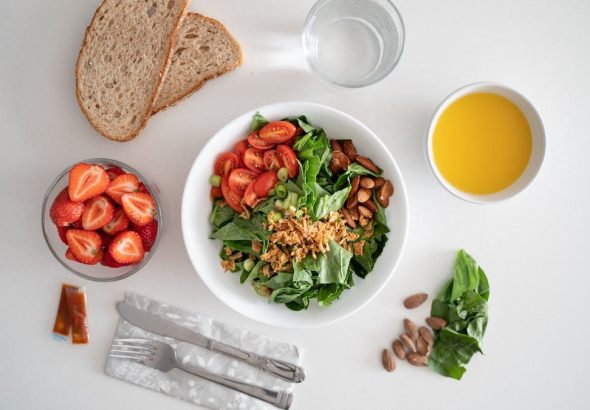 Top view of a healthy salad and fresh ingredients with bread and juice on a white surface.