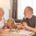 Grandparents and a child bond over painting at a cozy home setting, smiling and focused.