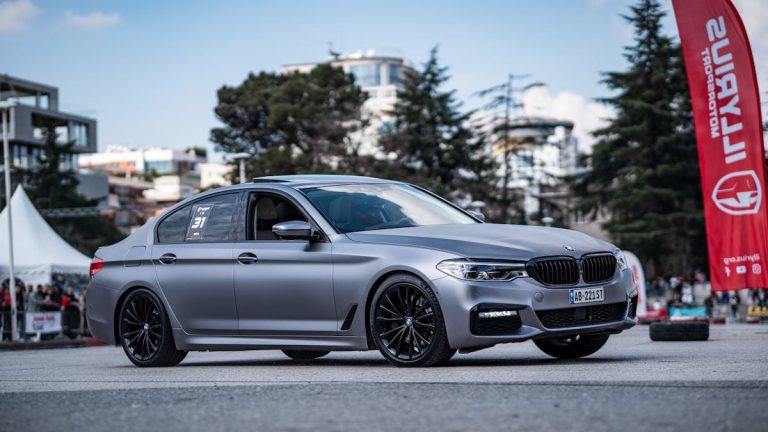 A stylish silver BMW parked on a city street during a car event, showcasing modern design.